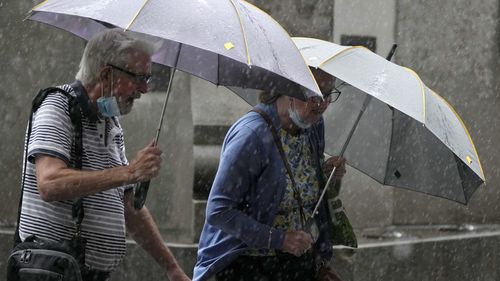 Pedestrians use umbrellas to keep out the rain in Sydney, Wednesday, March 2, 2022, as parts of Australia's southeast coast were inundated by the worst flooding in over a decade.  Flood waters are moving south into the New 