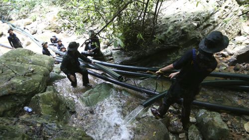 Thai soldiers drag water pipes to bypass water away from the cave. Picture: AAP