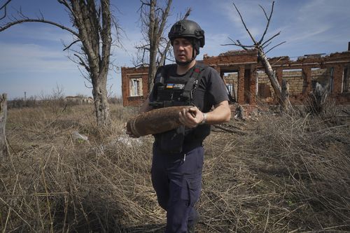 A Ukrainian Emergency Situation sapper carries an unexploded shell after using a mine-clearing machine to clear the site of explosives after battles with Russian troops, near Balaklia, Kharkiv region, Ukraine, Monday, April 1, 2024.