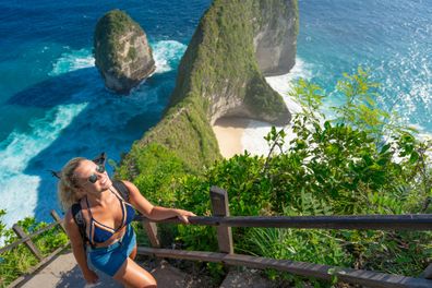 Young female tourist visiting Kelingking Beach on the Indonesian island of Nusa Penida. Climbs up the step trail to the top.