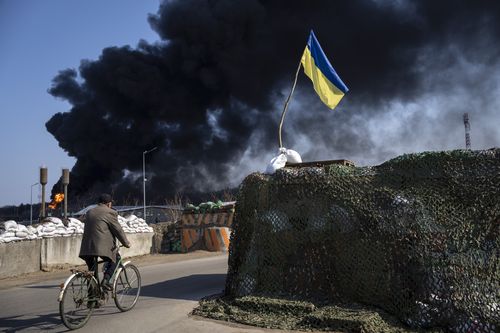 A man rides a bicycle as black smoke rises from a fuel storage of the Ukrainian army following a Russian attack, on the outskirts of Kyiv, Ukraine, Friday, March 25, 2022 