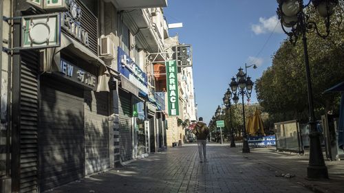 FILE - A man walks past closed shops in Tunis' landmark Avenue Habib Bourgiba, where massive protests took place in 2011, on the tenth anniversary of the uprising, during to a national lockdown after a surge in COVID -19 cases, in Tunis, Thursday, Jan. 14, 2021. Despite an election debacle, Tunisia's increasingly authoritarian president appears determined to upend the country's political system, threatening to unravel the fragile democracy and collapse the economy in the North African nation tha