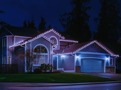 Night time photo of a modern American suburban home decorated with festive Christmas holiday lights and red ribbons on garage doors