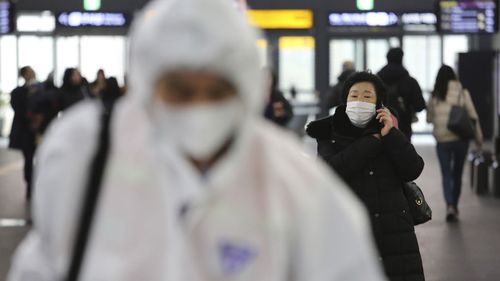 A woman wears a mask as an employee works to prevent a new coronavirus at Suseo Station in Seoul, South Korea, Friday, Jan. 24, 2020.