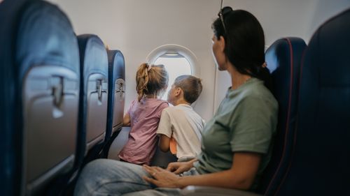 Mother with two children, son and daughter  traveling by plane, kids are looking through window