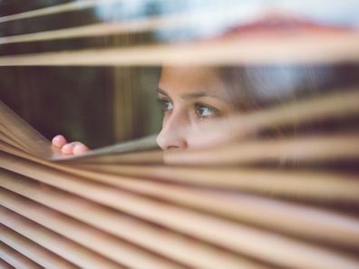 Woman looking through blinds in house