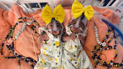 Premature twins in yellow outfits hooked up to machines in the NICU.