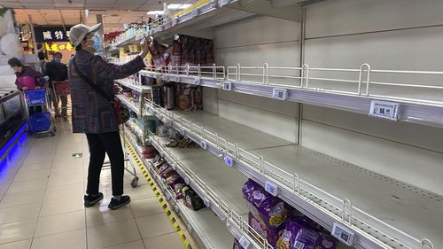 Una mujer compra en un supermercado de Beijing con algunos estantes casi vacíos en el pasillo de fideos instantáneos mientras los residentes se abastecen a medida que los vecindarios se cierran. 