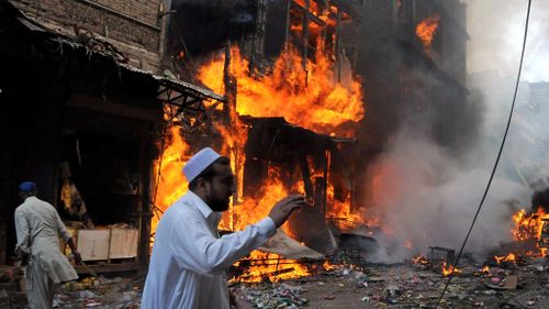 A Pakistani man runs past burning shops at a market following a deadly car bomb blast in Peshawar. (Getty)