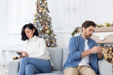 A young couple, a man and a woman, are sitting at home on the sofa on different sides and using phones.