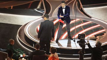 Denzel Washington talks to Chris Rock  onstage after the presenter was struck by Will Smith.