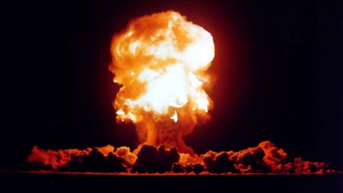 A nuclear bomb explodes, sending a mushroom cloud up into the sky.