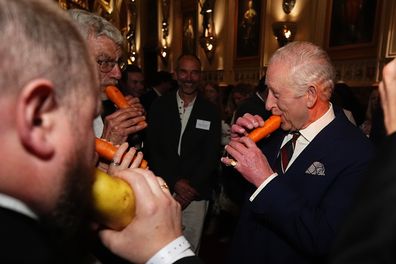 WINDSOR, ENGLAND - APRIL 3: King Charles III plays a carrot with the London Vegetable Orchestra during a reception to recognise those involved in community music across the UK, at Windsor Castle on April 3, 2025 in Windsor, England. The 350 guests include leaders of community music groups and music-related projects, many of whom are volunteers. (Photo by Aaron Chown - WPA Pool/Getty Images)