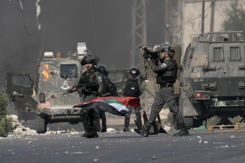 Israeli bored policeman holds a Palestinian flag he took from Palestinians during clashes following a demonstration in support of the Gaza Strip in the West Bank city of Nablus, Friday, Oct. 13, 2023.