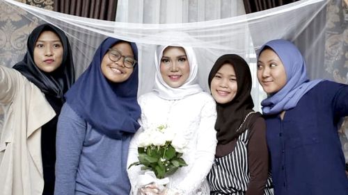 Intan Syari in her wedding dress with friends holding up her veil.