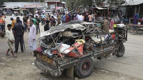 People stand near the wreckage of a bus that fell into a roadside ditch in Shibchar area in Madaripur district, Bangladesh, Sunday, March 19, 2023. 