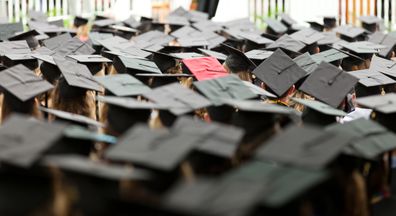 A red mortar hat in a sea of black ones at a college graduation.