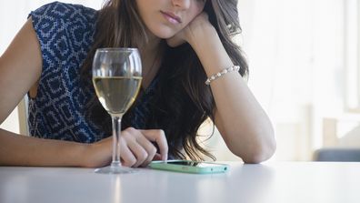 Woman looking at phone with glass of wine