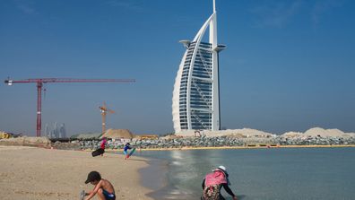 Families play on a public beach with the Burj al-Arab hotel behind them in Dubai, United Arab Emirates, Friday, May 29, 2020