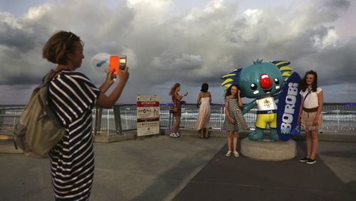 Children pose for the photographs with Commonwealth Games mascot Borobi at Surfers Paradise Beach as clouds linger behind them. (AAP)