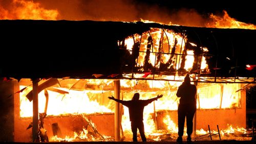 Protesters take their pictures in front of the burning Juanita's Fashion R Boutique on West Florissant Avenue in St. Louis. (AAP)