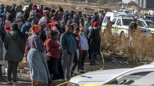 People look on at the scene of an overnight bar shooting in Soweto, South Africa.
