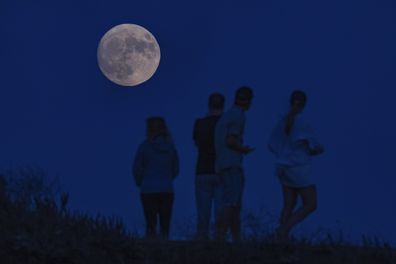 Visitors stop to take pictures of a waxing gibbous moon at 96% illumination at Fort Baker in Sausalito, Calif., on Tuesday, Aug. 29, 2023.