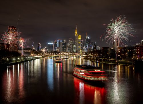 Party boats cruise over the river Main with only a few fireworks near the buildings of the banking district in Frankfurt, Germany, early Saturday, Jan. 1, 2022. 