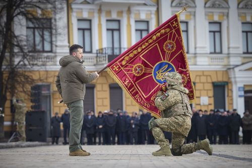 Ukrainian President Volodymyr Zelenskyy, left, holds the flag of a military unit as an officer kisses it, during commemorative event on the occasion of the Russia Ukraine war one year anniversary in Kyiv, Ukraine, Friday, Feb. 24, 2023 