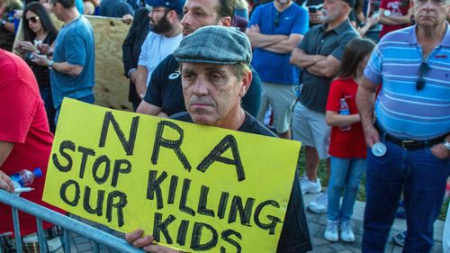 A man holds an anti-NRA sign at a vigil for victims of a mass shooting that took place at Marjory Stoneman Douglas High. (AAP)