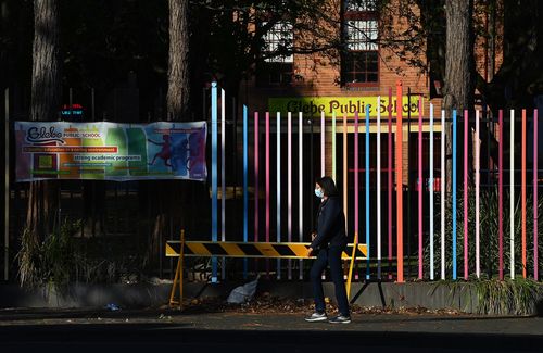 A woman wearing a face mask walks past Glebe Public School during the city wide COVID-19 lockdown. Glebe, NSW. 22nd September, 2021. Photo: Kate Geraghty