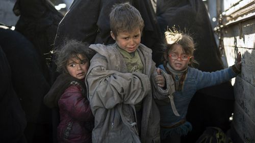 Women and children exit the back of a truck as they arrive at a screening area after being evacuated out of Baghouz.