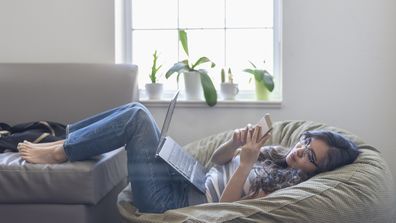 Woman on bean bag uses laptop and mobile phone