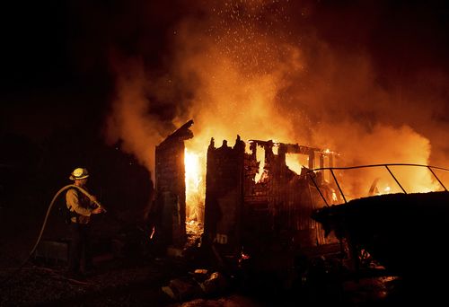 Firefighter Jay Wilkens monitors a flaming shed and boat as the Holiday fire burns in Goleta, Calif., on Saturday, July 7, 2018. (AP Photo/Noah Berger, File)