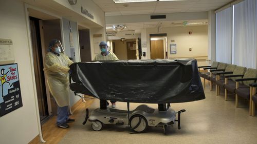 Hospital staff members enter an elevator with the body of a COVID-19 victim on a gurney at St. Jude Medical Center in Fullerton, California. The state's death count from the coronavirus surpassed 15,000 yesterday even as the state saw widespread improvement in infection levels.