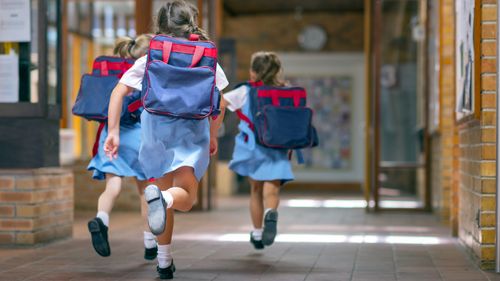 Rear view of excited students running towards entrance. Girls are carrying backpacks while leaving from school. Happy friends are wearing school uniforms.