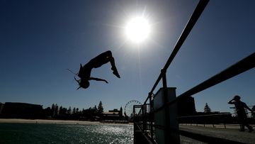 Beachgoers are seen jumping off a jetty at Glenelg Beach in Adelaide.