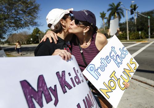 Lauren Duck, right, hugs Debby Stout, left, as they stand on a street corner holding up anti-gun signs. (AAP)