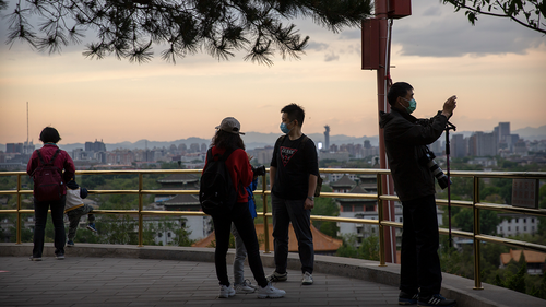 People wearing face masks to protect against the spread of the new coronavirus stand on a hilltop at a public park in Beijing, Saturday, April 25, 2020. 