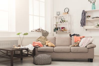 Sofa in messy living room with many stack of clothes. Disorder and mess at home, copy space