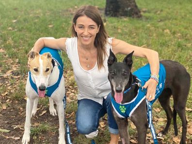 Dr. Katrina kneeling down hugging two greyhounds on either side of her.