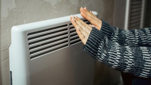 Woman holding hands to heater winter bills energy prices living in poverty cold weather