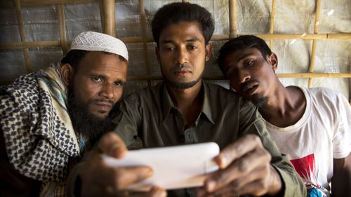 Rohingya Muslim refugee Mohammad Karim, 26, center, shows a mobile video of Gu Dar Pyin's massacre to other refugees in Kutupalong refugee camp, Bangladesh. (AAP)
