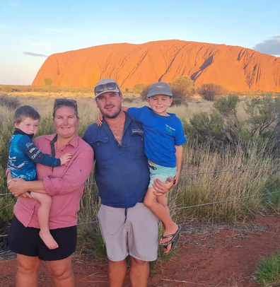 Mum, dad and two kid pose in front of Uluru at sunset
