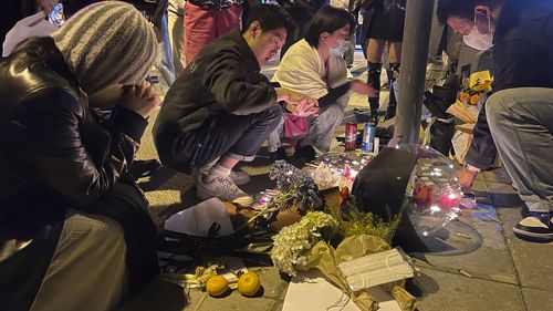 Residents mourn for the victims of a recent deadly fire at a residential building in Urumqi city at a road sign of the Middle Wulumuqi Road or Middle Urumqi Rd in Shanghai, China.