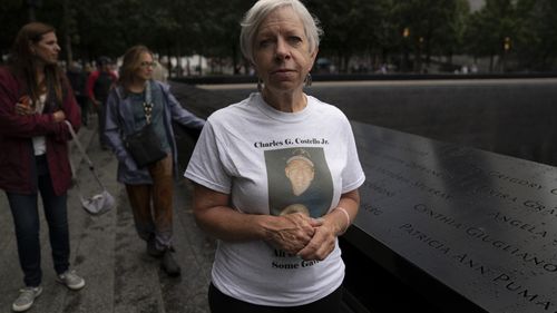 Kathy Birch, sister of Charles Gregory "Chuck" Costello Jr., an elevator electrician who ran into Tower 1 of the World Trade Center before the towers fell, stands beside her brothers name while visitors browse the north pool at the National September 11 Memorial & Museum in New York.