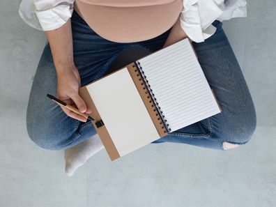 Top view of a pregnant woman sitting cross-legged with a notebook on her lap.