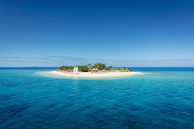 Beautiful small island in the middle of the south pacific ocean with beach huts, lounge chairs, palm trees, surrounded with beautiful clear turquoise water. Islet, Mamanuca Islands, Fiji, Melanesia