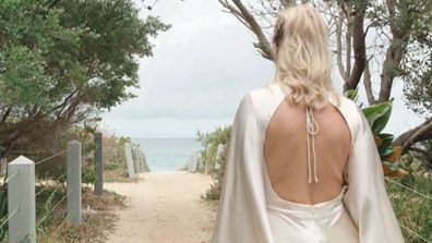 A bride appears to walk on sand with an open-back wedding dress to meet her groom.