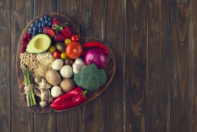 Healthy food on a heart shape cutting board. Love of food concept with fruit, vegetables, grains and high fibre foods. Rustic wood textures